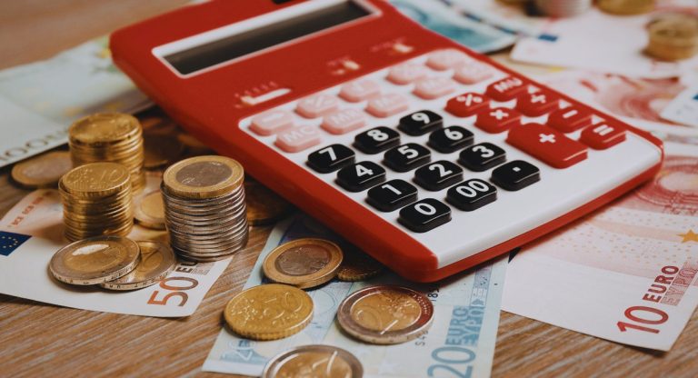 Calculatrice rouge posée sur des billets et pièces d'euros pour calculer un salaire