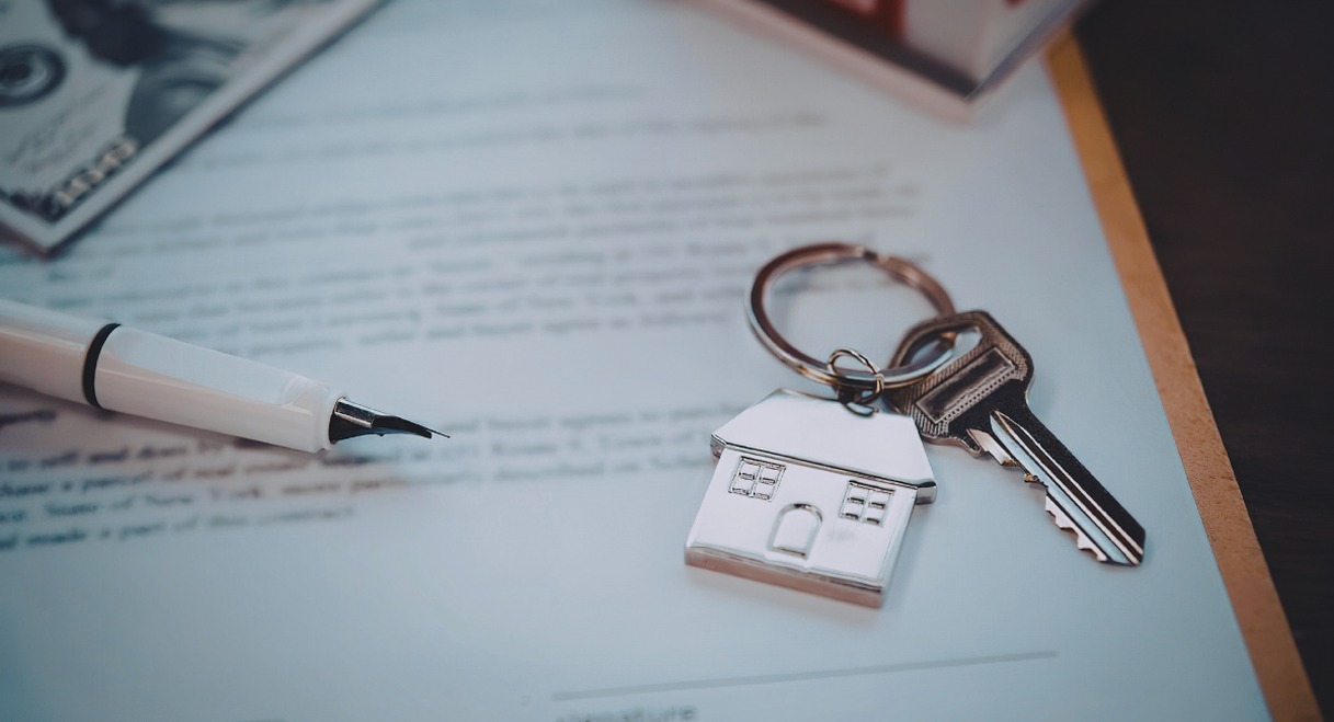 Contrat immobilier signé avec une clé en forme de maison posée dessus