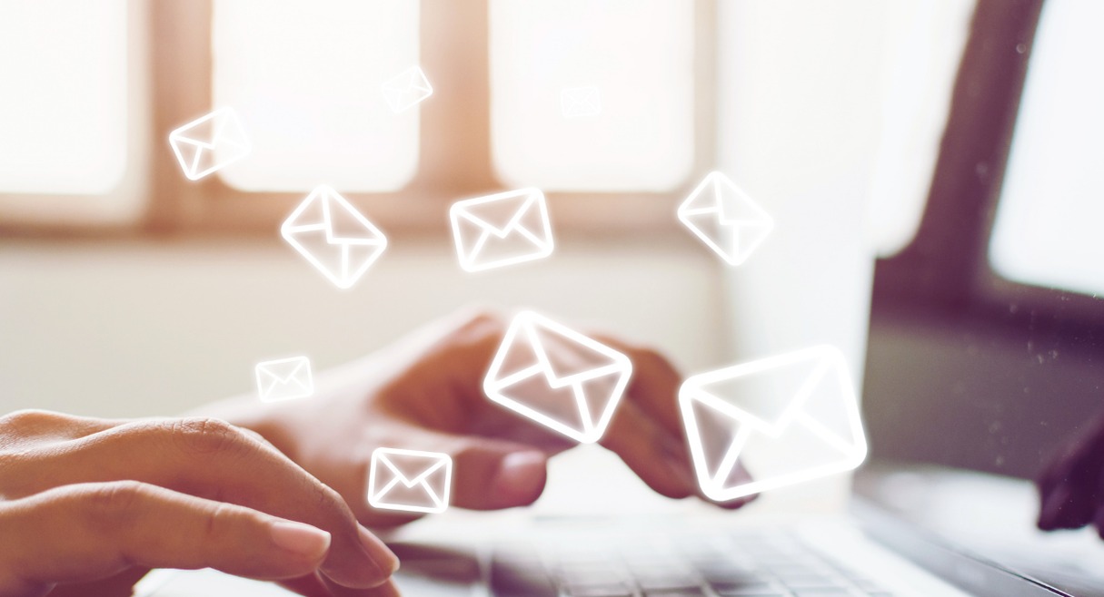 Mains sur un clavier d'ordinateur avec des icônes d'enveloppes d'email qui s'envolent