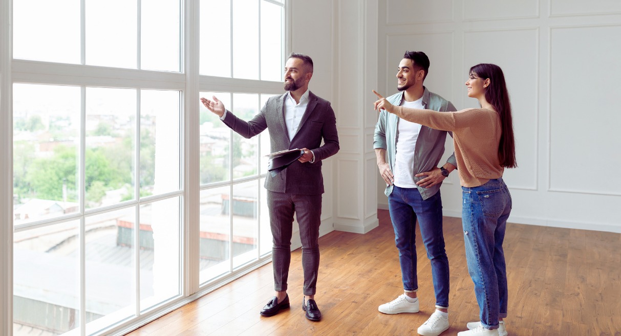 Agent immobilier montrant un appartement lumineux à un couple de jeunes acheteurs