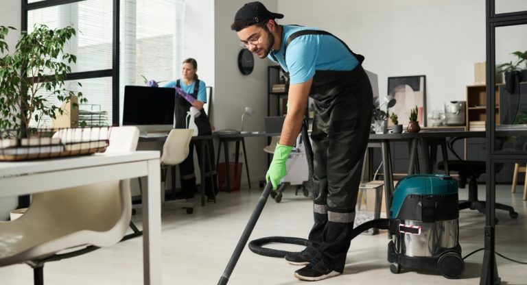 Deux agents de nettoyage professionnels entretiennent un espace de bureaux, l'un passant l'aspirateur