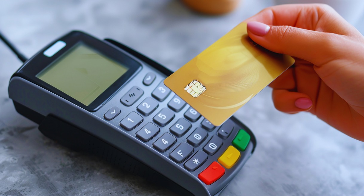 Main tenant une carte bancaire dorée devant un terminal de paiement