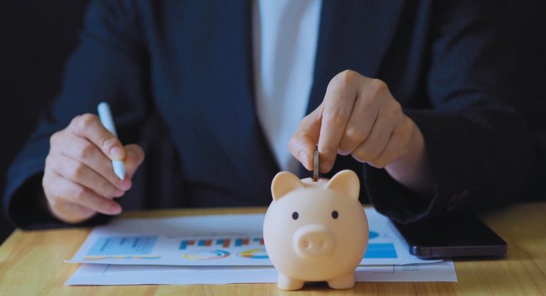 Personne déposant une pièce dans une tirelire cochon à côté de graphiques financiers