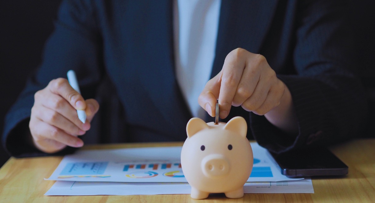 Personne déposant une pièce dans une tirelire cochon à côté de graphiques financiers