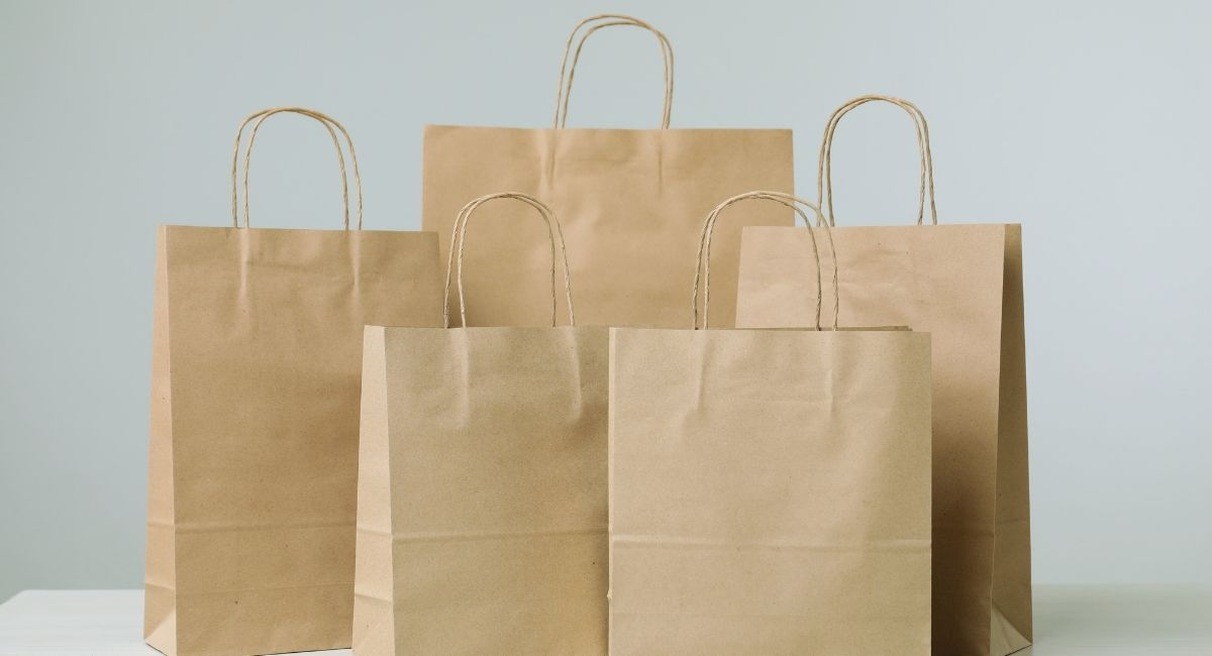 Cinq sacs en papier kraft à poignées torsadées de tailles différentes posés sur une table claire