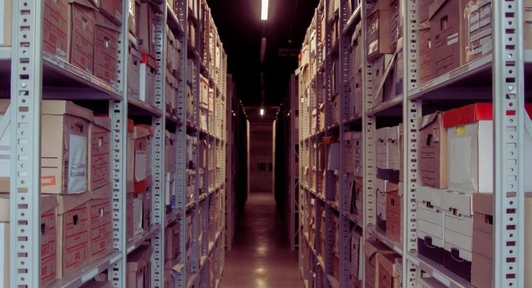 Allée d'un entrepôt d'archives avec des rayonnages métalliques chargés de boîtes en carton