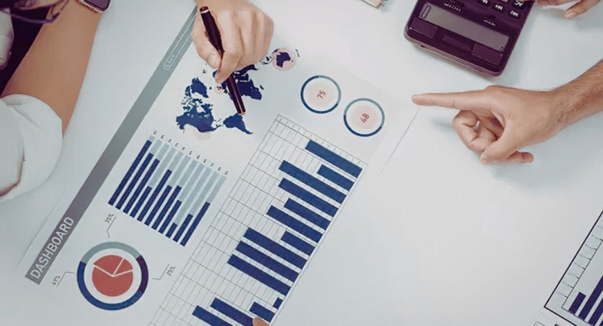 Mains pointant des graphiques en barres et une carte du monde sur un tableau de bord imprimé posé sur une table